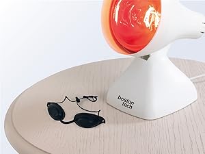 con bombilla roja iluminada. En la base se lee «Lexon Design». Gafas de sol negras visibles sobre una superficie de madera clara junto